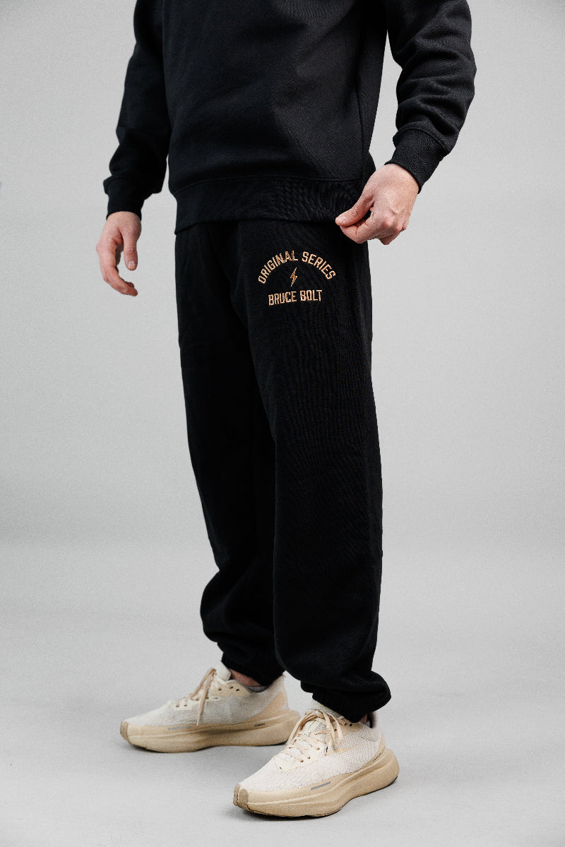 Person wearing black sweatpants with text and a lightning bolt design on a gray background